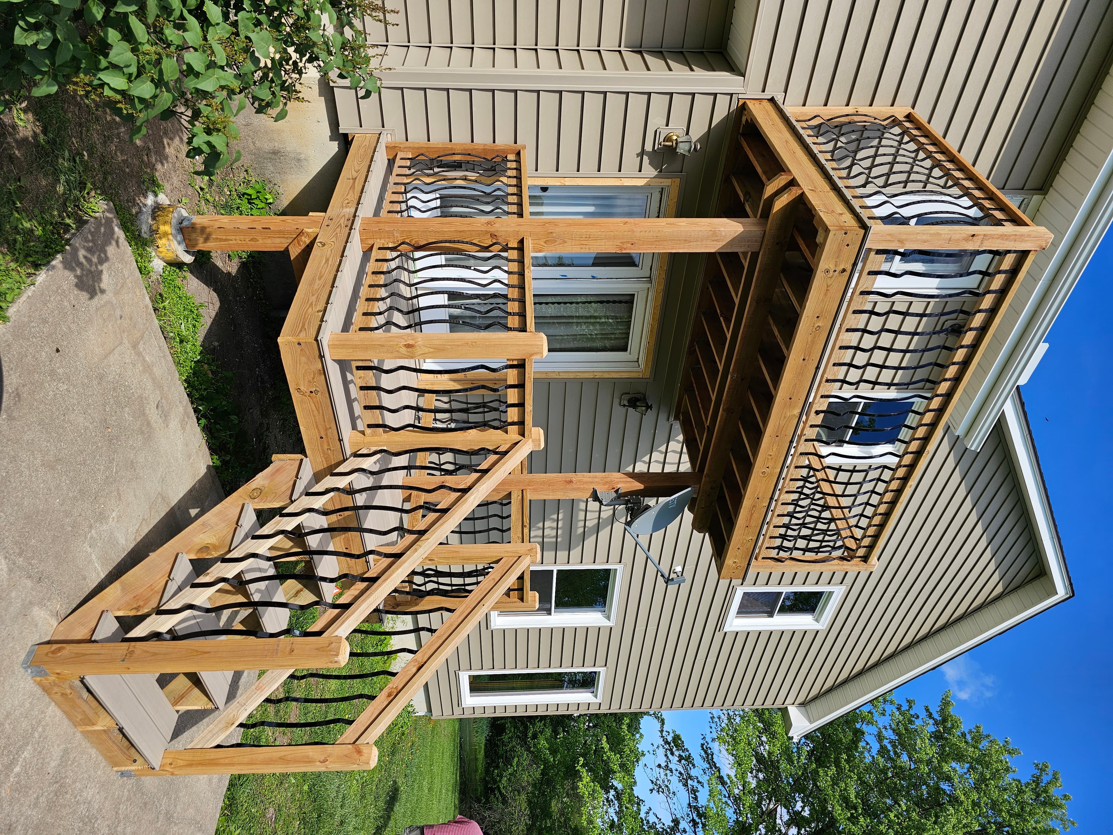 Two-level residential wood deck with stairs and black metal balusters.