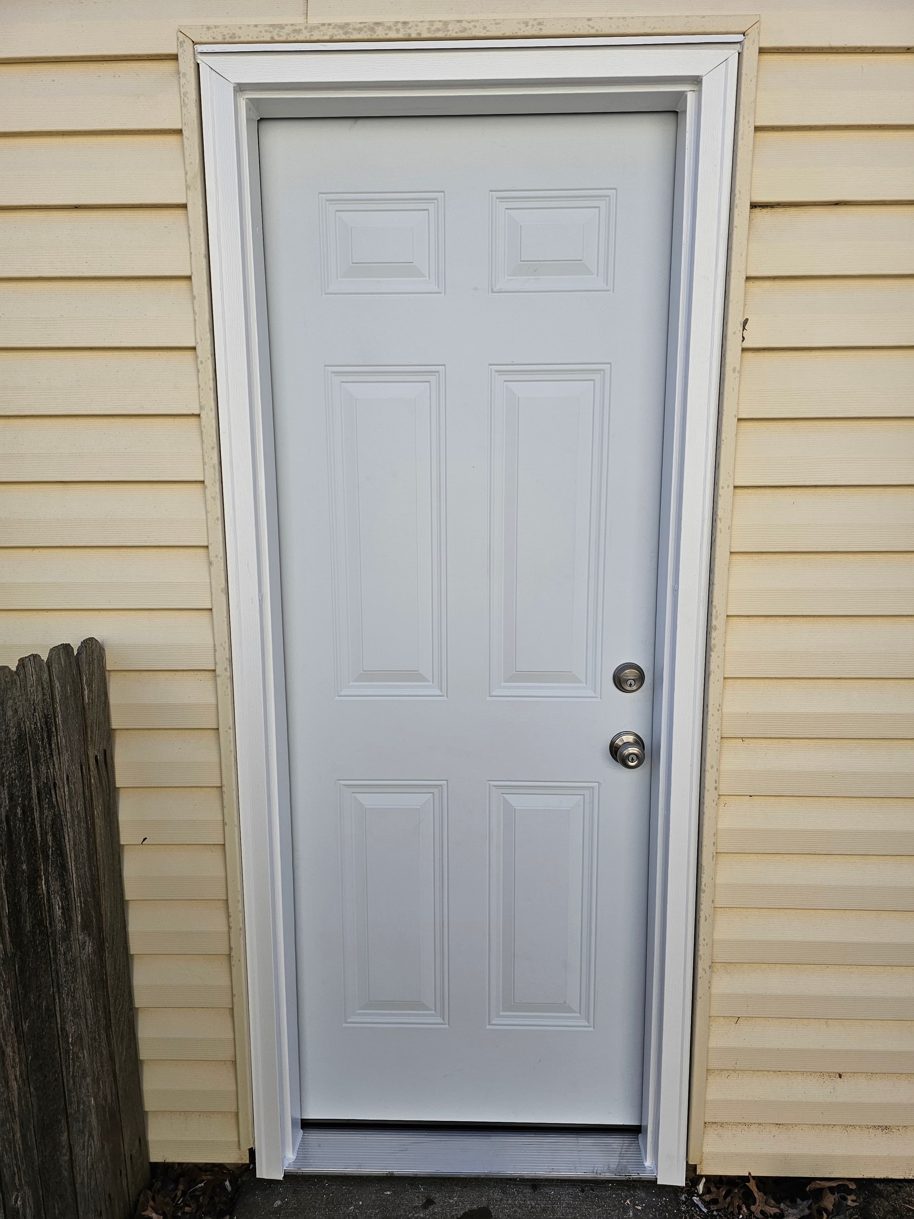 White exterior entry door with new trim and threshold on light-colored siding.