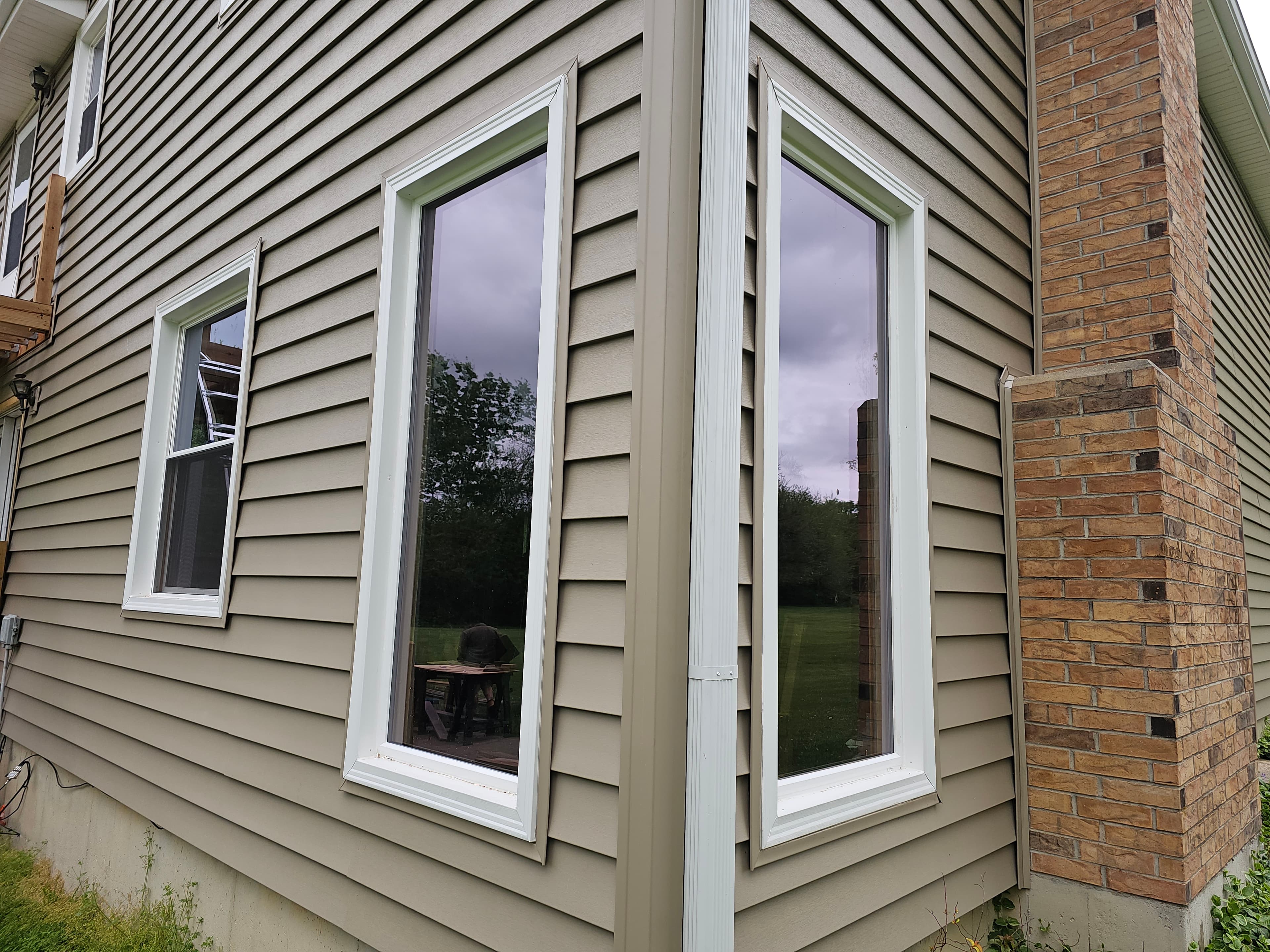 Residential exterior wall with newly installed white-trim replacement windows beside brick chimney.